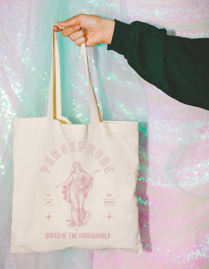 A cotton canvas totebag featuring various goddess designs including Demeter, Persephone, Aphrodite, Artemis, and Athena. The totebags come in shades of pink, gold, red, and black, of each goddess.