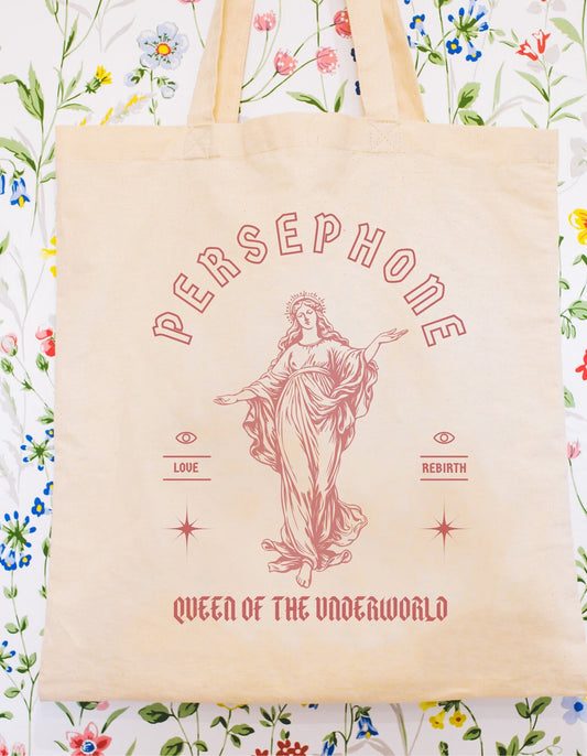 A cotton canvas totebag featuring various goddess designs including Demeter, Persephone, Aphrodite, Artemis, and Athena. The totebags come in shades of pink, gold, red, and black, of each goddess.